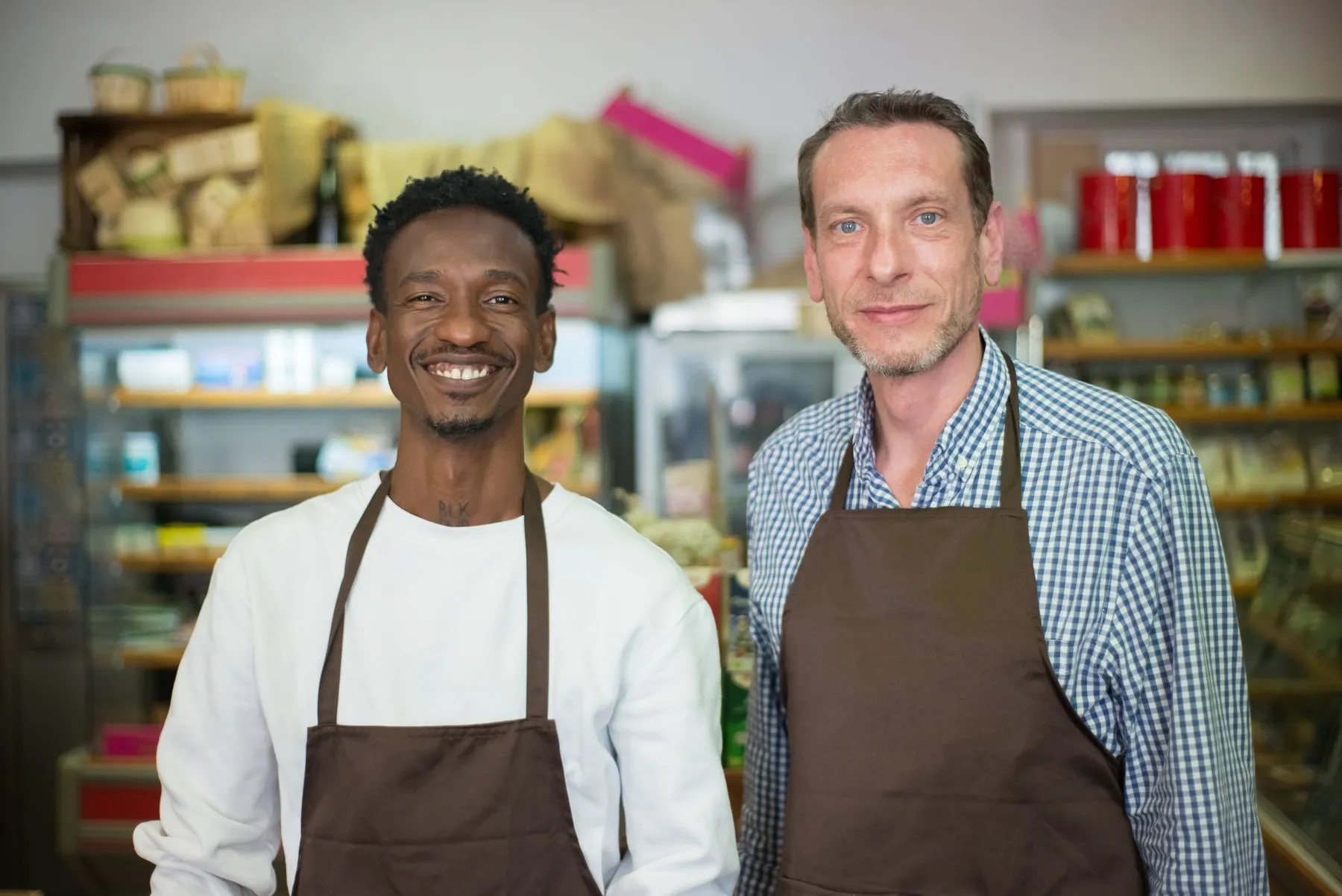Dois sócios de avental sorrindo em frente ao próprio comércio