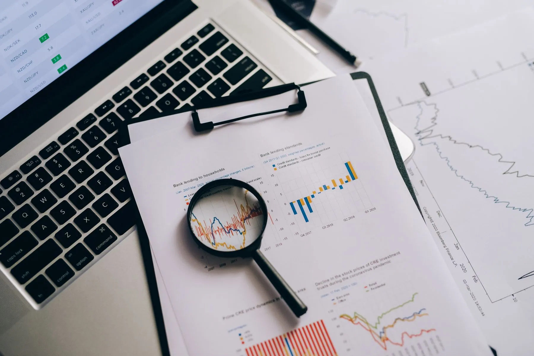 Lupa sobre relatórios e gráficos ao lado de um notebook